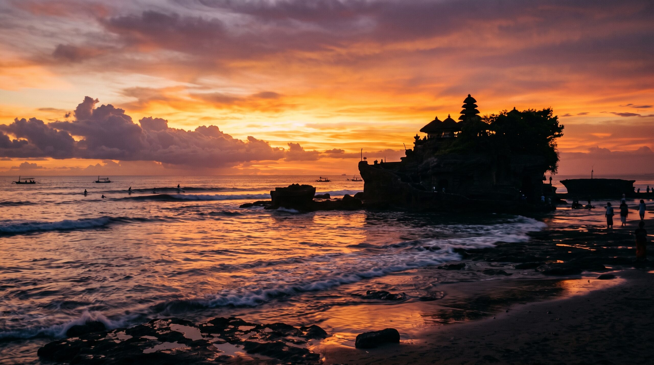 Tanah Lot temple at golden hour during Bali's dry season with surfers offshore